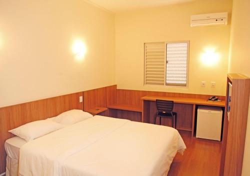 a bedroom with a bed and a desk and a window at Bernal Hotel Econômico in Ituiutaba