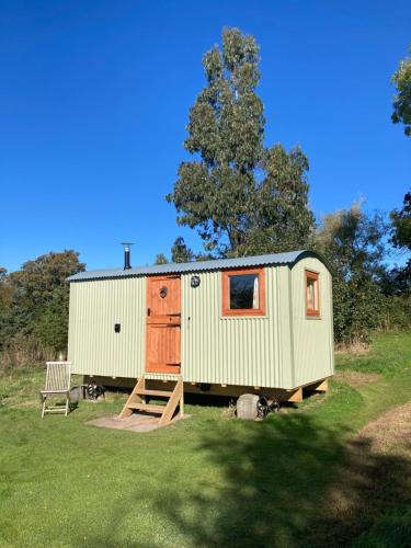 a green tiny house sitting on top of a field at The Dragon's Hut with cozy logburner in Wrexham