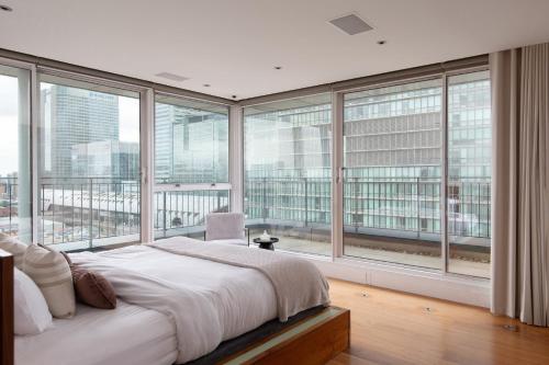 um quarto com uma cama grande e janelas grandes em The Canary Wharf Secret - Glamorous 3BDR Flat with Terrace and Parking em Londres