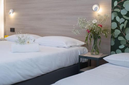 2 camas con almohadas blancas y un jarrón de flores sobre una mesa en Hub Hotel, en Gubbio