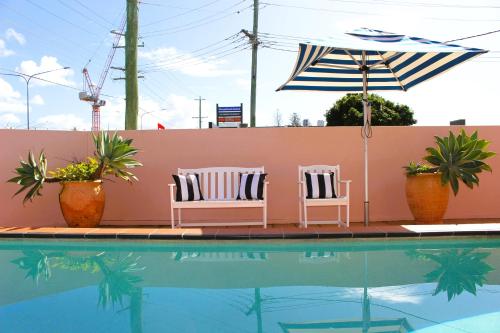 2 sillas y sombrilla junto a la piscina en Camden Motor Inn, en Gold Coast