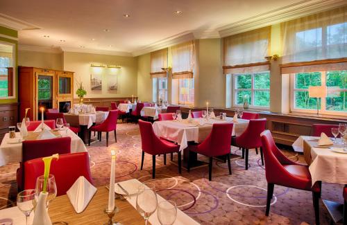 ein Restaurant mit Tischen, roten Stühlen und Fenstern in der Unterkunft Leonardo Hotel Hamburg Stillhorn in Hamburg