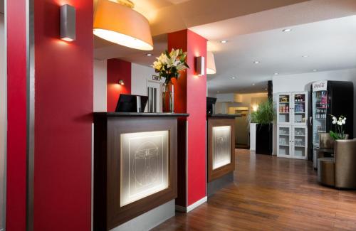 a lobby with red walls and a counter with flowers at Leonardo Hotel Frankfurt City Center in Frankfurt