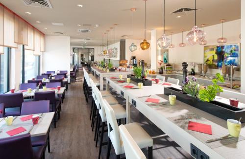 un restaurante con mesas blancas y sillas moradas en Leonardo Hotel Munich City Olympiapark, en Múnich