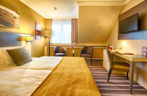 a hotel room with a bed and a desk and chairs at Leonardo Hotel Heidelberg Walldorf in Walldorf