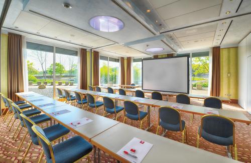 a conference room with a long table and chairs and a screen at Leonardo Hotel Köln in Cologne