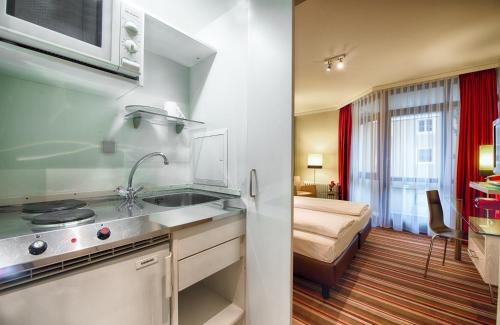 eine Küche mit einem Waschbecken und ein Bett in einem Zimmer in der Unterkunft Leonardo Hotel & Residenz Muenchen in München