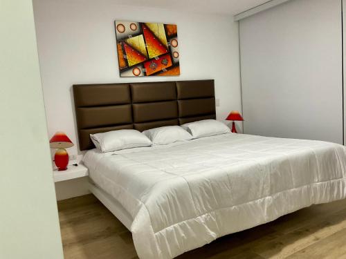 a bedroom with a large white bed with a painting on the wall at Solymar Beach House - Paracas in Paracas