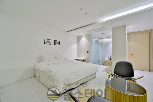 a white bedroom with a bed and a black chair at Golden Hotel Incheon in Incheon