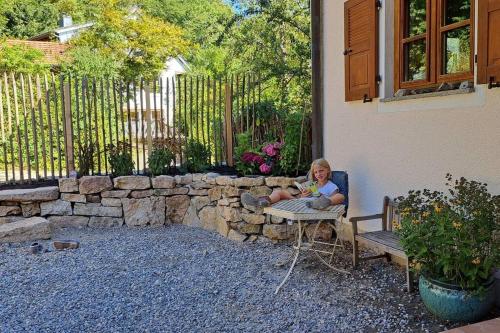 a woman sitting in a chair in front of a stone wall at Gemütliche Waldrandlage in Badenweiler Sehringen Ferienwohnung in Badenweiler