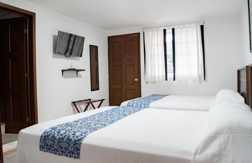 a white bedroom with two beds and a tv at Hotel Rio Atlixco in Atlixco