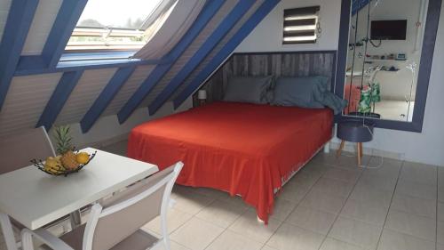 - une chambre avec un lit doté d'une couverture rouge et d'une table dans l'établissement Paradise chez Nono, à Baie-Mahault