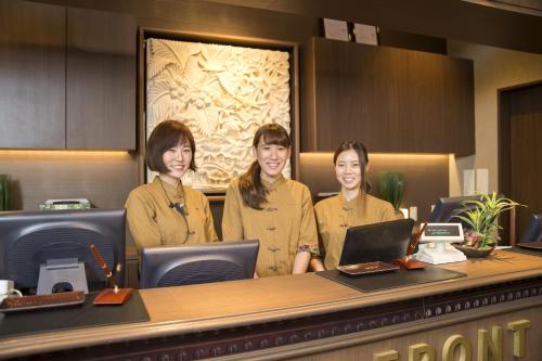 three women are standing in front of a laptop computer at Capsule Hotel Anshin Oyado Shinjuku in Tokyo