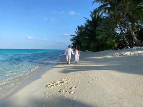 un homme et une femme se promenant sur la plage dans l'établissement Thoddoo Haisha inn, Maldives, à Thoddoo