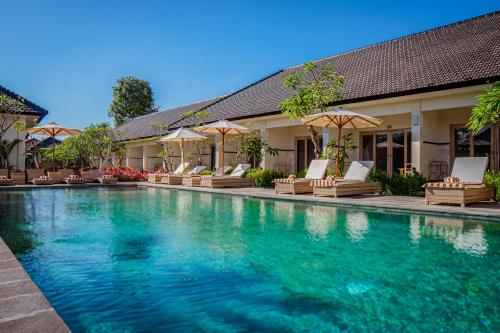 a swimming pool with chairs and umbrellas next to a building at Green D'mel Bali in Nusa Dua