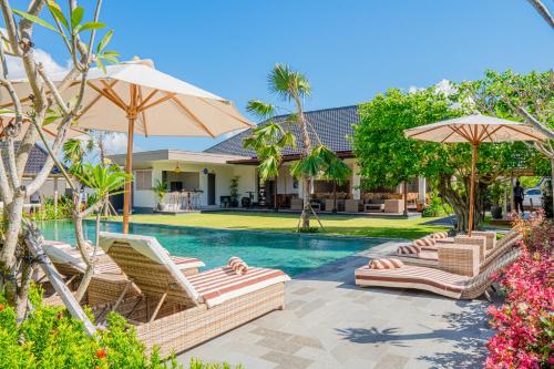 a swimming pool with lounge chairs and umbrellas at Green D'Mel Luxury Homestay in Nusa Dua