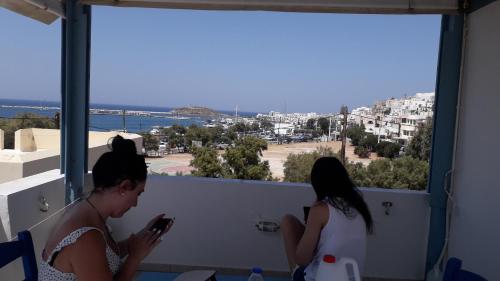 two women standing on a balcony looking at their cell phone at Katy's Home in Naxos Chora