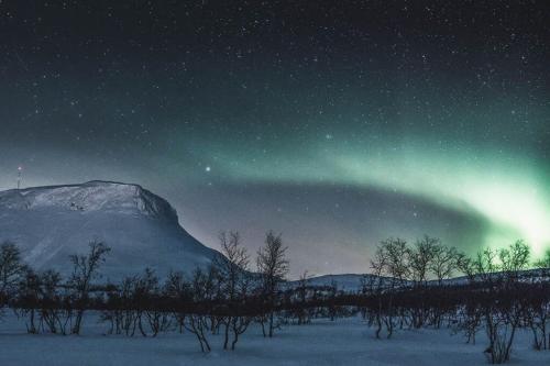 an aurora in the sky at night with a mountain at Santa's Hotel Rakka in Kilpisjärvi