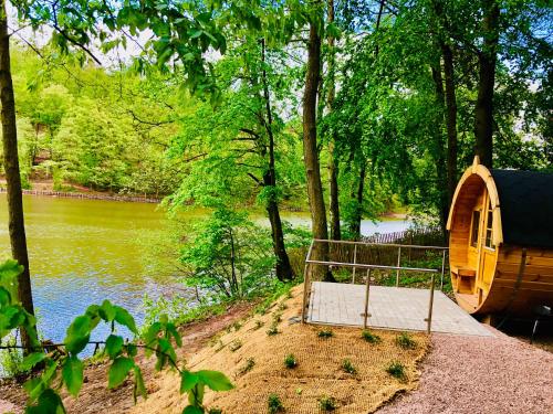 a wooden cabin next to a river with trees at Ferienwohnungen & Campingfässer am Kunstteich in Wettelrode