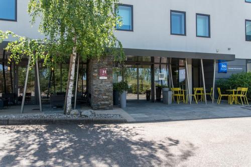 a building with tables and chairs in front of it at Ibis Budget Archamps Porte de Genève in Archamps