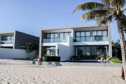 a house on the beach with a palm tree at Faru Beachfront Villa Sanctuary Ho Tram in Ho Tram