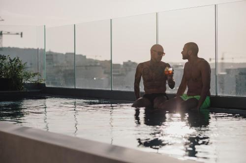 dois homens sentados na água numa piscina em ibis Styles ST Pauls Bay Malta em St. Paul's Bay