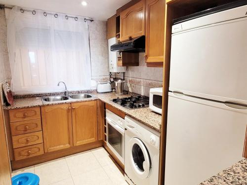 een keuken met houten kasten en een witte koelkast bij Apartamento en 7ᵃ Planta - 1ᵃ Línea de Playa - Bahía Park, Marina d'Or in Oropesa del Mar