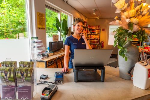 a woman talking on a phone at a desk with a laptop at Comfort Rooms by EuroParcs De Hooge Veluwe in Arnhem