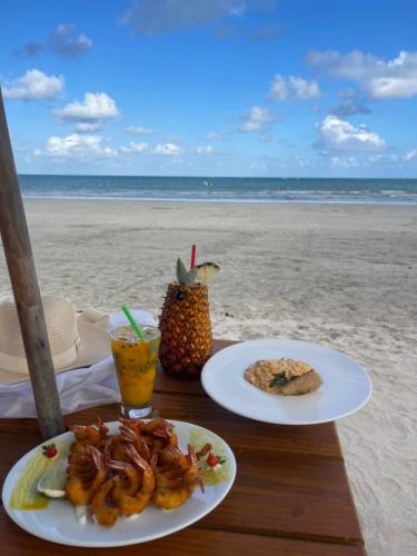 einen Tisch mit zwei Tellern Essen am Strand in der Unterkunft Casa Blanca Hibiscus Angra de Ipioca Maceió in Maceió