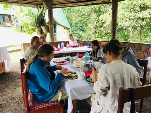 un grupo de personas sentadas alrededor de una mesa comiendo en Songota Falls Lodge, en Arusha