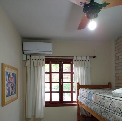 a bedroom with a bed with a ceiling fan and a window at Apartamento Bombinhas in Bombinhas