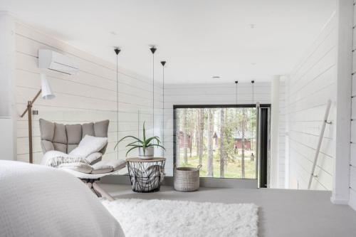 a white bedroom with a chair and a window at Polaris Villas in Muonio
