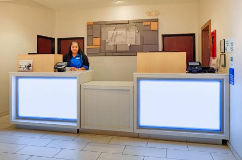 una mujer parada en un mostrador con dos carteles en blanco en Holiday Inn Express Hotel & Suites Burleson - Fort Worth, an IHG Hotel, en Burleson