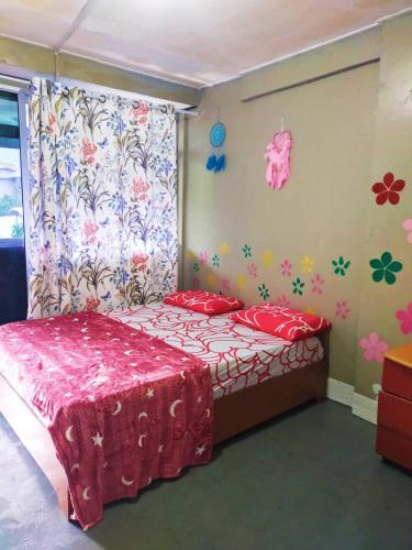 a bedroom with a bed with a red bedspread and flowers on the wall at Dreamcatcher Homestay, Kundasang in Ranau