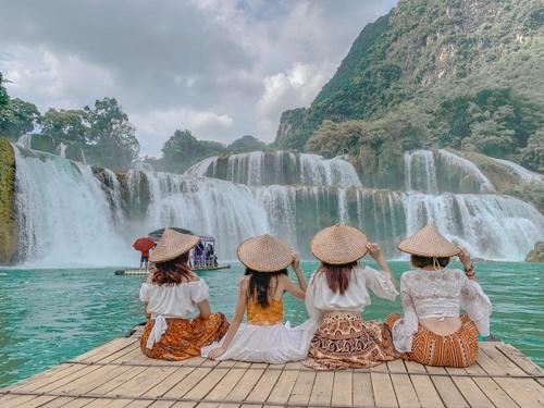 3 Mädchen sitzen auf einem Pier vor einem Wasserfall in der Unterkunft Khách sạn Hoàng Trang in Cao Bằng
