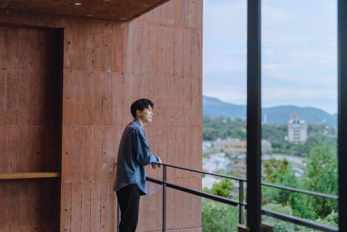 a man standing on a balcony looking out at the city at SEKIYA RESORT Galleria Midobaru in Beppu