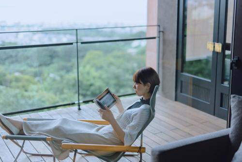 a woman sitting in a chair reading a book on a balcony at SEKIYA RESORT Galleria Midobaru in Beppu
