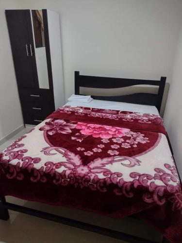 a bed with a red and white comforter with flowers at HOSPEDAJE NELLY in Puerto Chicama