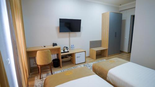 Una habitación de hotel con dos camas, un escritorio y un televisor. en Almalyk Plaza Hotel, en Olmaliq