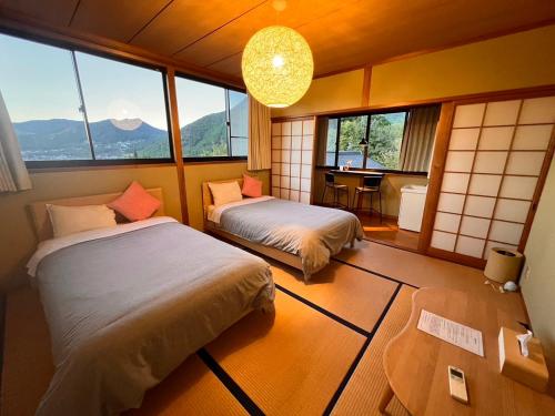 a room with two beds and a table and windows at 湯布院 星の里 Yufuin Hoshinosato in Yufuin