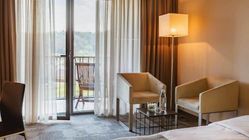 a hotel room with a bed and two chairs and a balcony at Terme Olimia - Hotel Sotelia in Podčetrtek