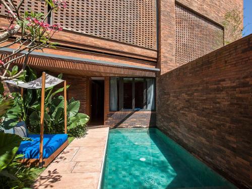 a swimming pool in front of a building with a brick wall at Potato Head Suites & Studios in Seminyak