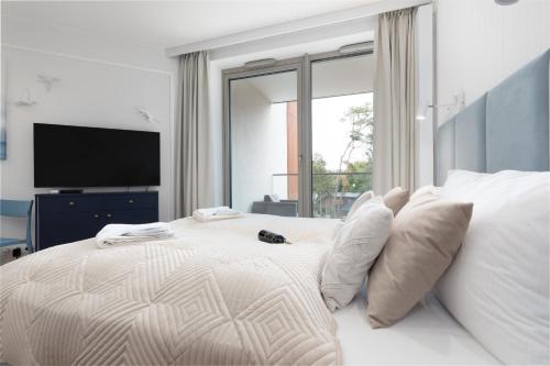 a white bedroom with a large bed with a television at Apartments Mazowiecka Pobierowo by Noclegi Renters in Pobierowo