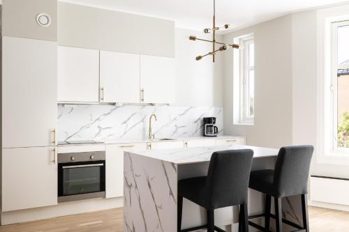a white kitchen with a marble counter and chairs at Frogner House - Uranienborg in Oslo