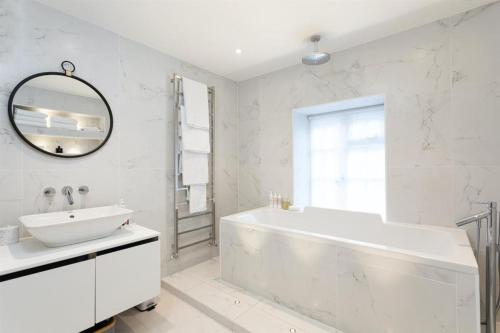 a white bathroom with a tub and a mirror at Stylish Home - Wentworth, Sunningdale Golf Club in Sunninghill