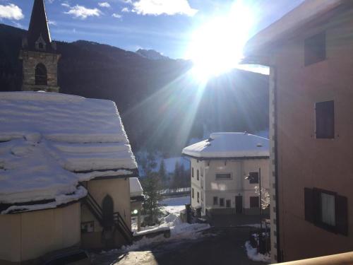 a sun shines behind a building with snow on the roof at Appartamenti Sasso Rosso in Commezzadura