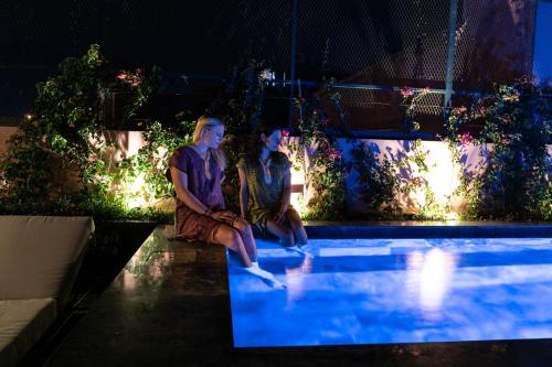 two people sitting next to a swimming pool at night at Riad Wazani Square & SPA in Marrakesh
