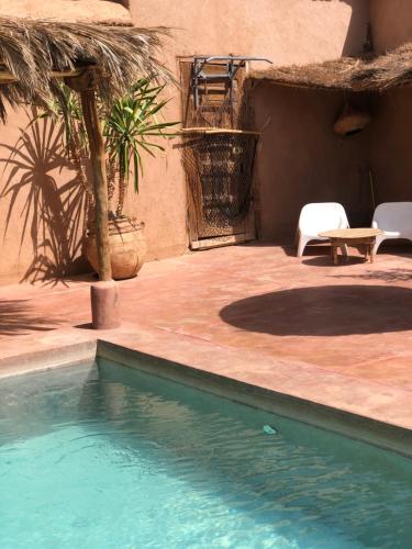 a swimming pool next to a patio with a table and chairs at Maison d'Hôtes Irocha in Tisselday