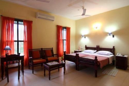 a bedroom with a bed and chairs and red curtains at Alps Residency in Madurai