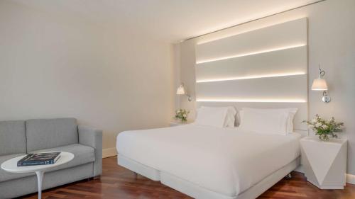 a bedroom with a white bed and a couch at NH Málaga in Málaga